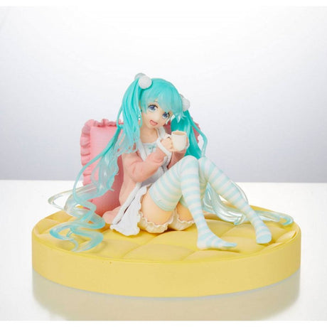 Figurine de Hatsune Miku en tenue pastel décontractée, assise avec une tasse dans les mains, ambiance cosy et kawaii.